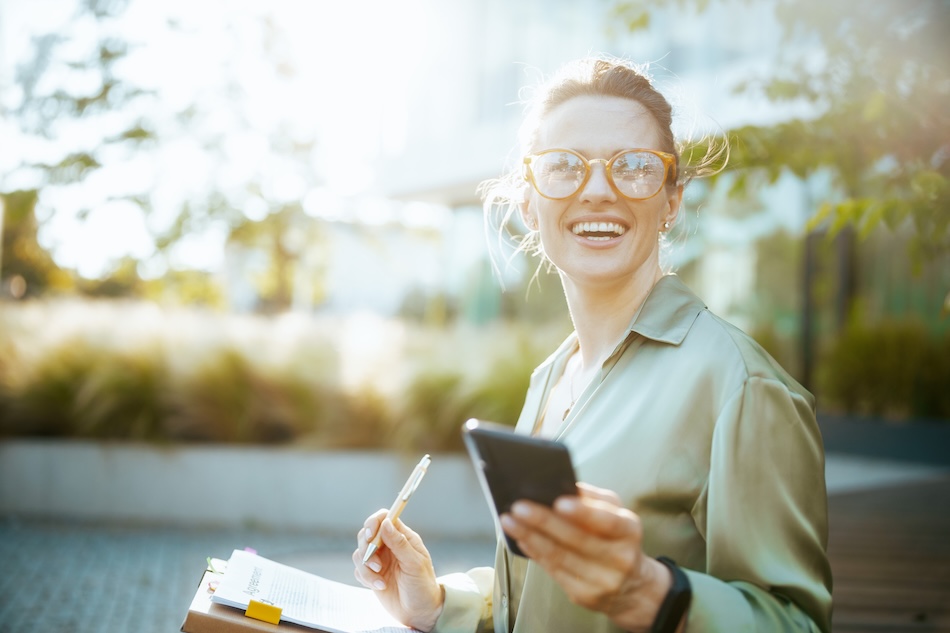 Femme souriante avec smartphone et carnet en extérieur